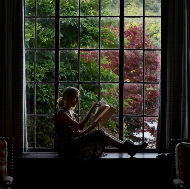 summer bucket list ideas: a woman is reading a book by the window